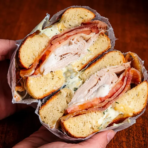 A sliced deli bagel sandwich with turkey, bacon and tomato